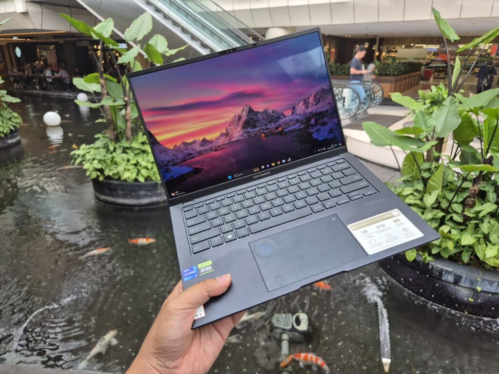 laptop ASUS ZenBook Pro 14 OLED (UX6404) dipegang dengan satu tangan dengan pemandangan taman di belakang