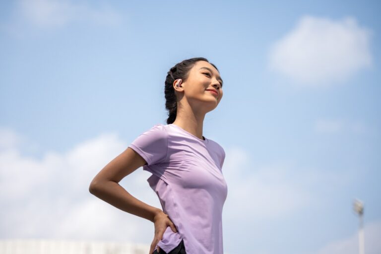 Wanita berbaju ungu menggunakan SHOKZ OpenFit Air